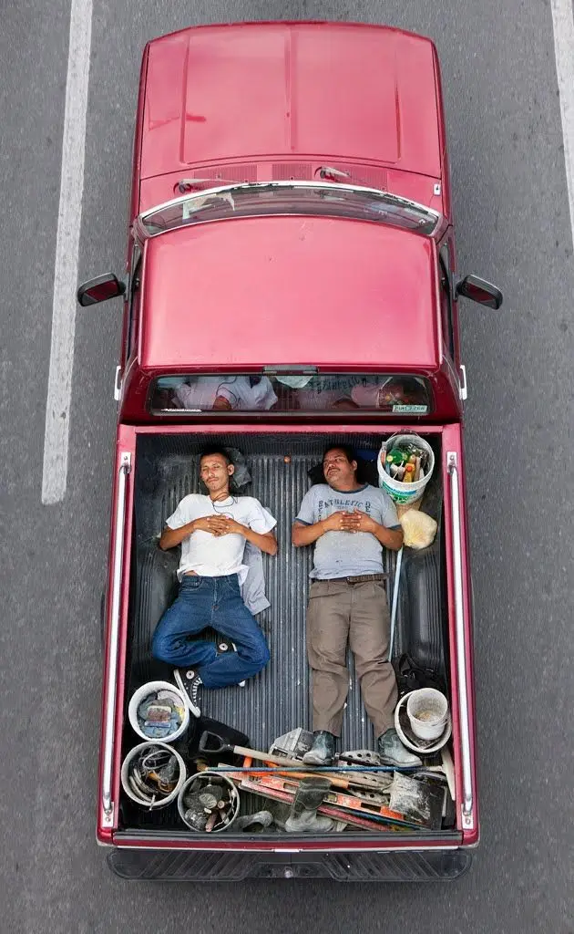High-angle view of two workers lying in bed of red pickup surrounded by tools