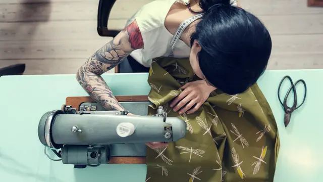 Tattooed Tailor Sewing Dragonfly-Print Fabric — Overhead Editorial Photo