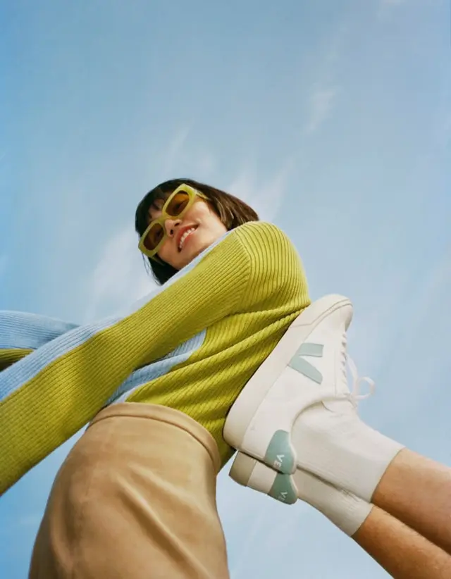 Low-angle lifestyle shot of white sustainable sneakers with mint 'V' logo — RRREVOLVE
