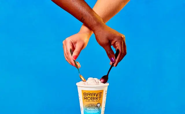 Brave Robot ice cream cup with two hands and spoons on bright blue backdrop