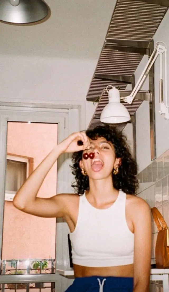 Candid summer portrait — woman with cherries in white crop tank and navy sweatpants