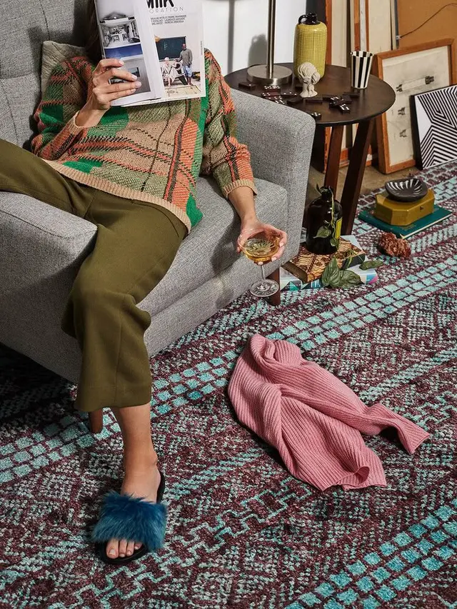 Eclectic living room styling with patterned rug, gray armchair, pink sweater
