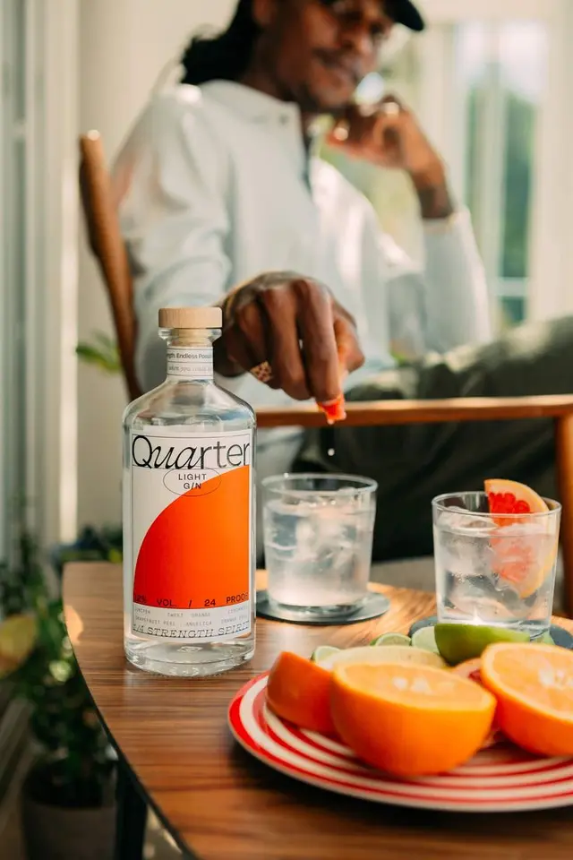 Quarter bottle and citrus cocktail setup — hand juicing limes on stainless bar