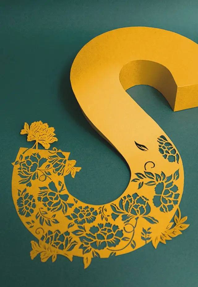 Golden yellow paper-cut letter S with ornate floral cutouts on teal background