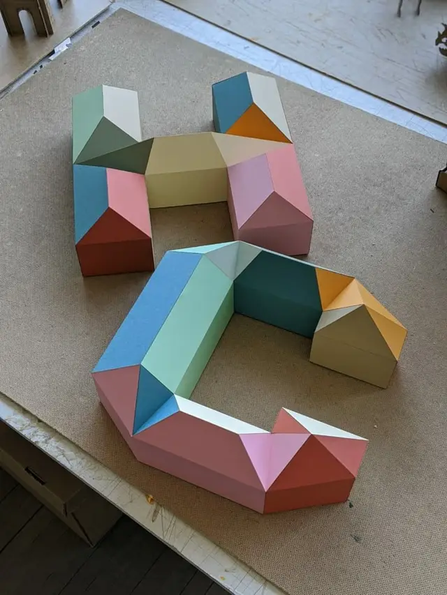 Pastel low‑poly paper letters H and C — folded cardstock sculpture