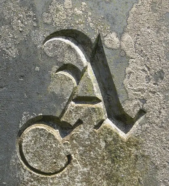 Weathered stone bas‑relief capital 'A' with moss and lichen