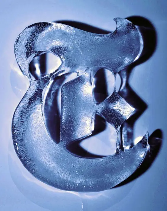 Translucent ampersand ice sculpture photographed in blue studio light