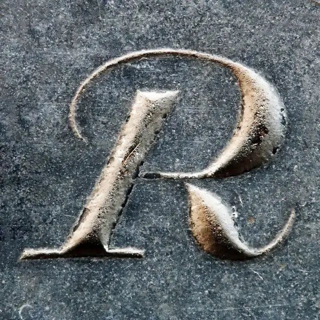 Close-up carved capital letter R in weathered dark stone