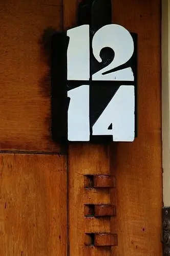 Black plaque with stacked white house numbers on warm wood door