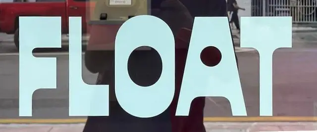 Storefront glass window with large pale-cyan 'FLOAT' vinyl lettering