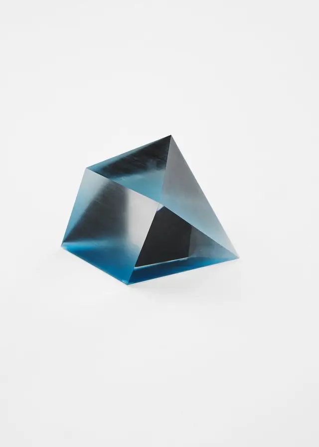Blue-tinted glass triangular prism on white studio background