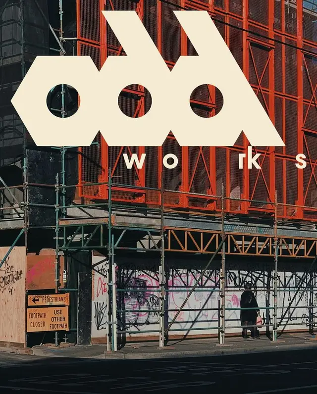 Scaffolded building with orange safety mesh and cream 'works' logo overlay