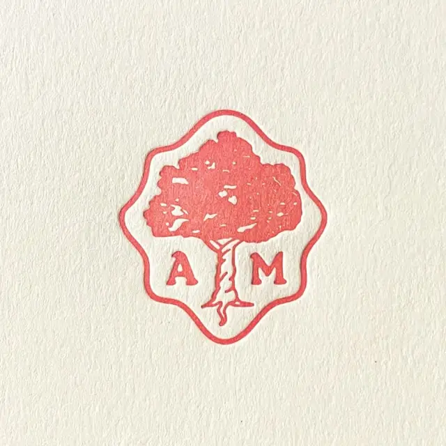 Letterpress tree monogram stamp (A M) — coral badge on cream paper