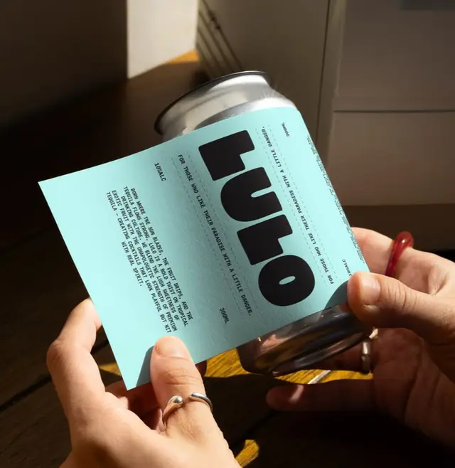 Hands applying pale turquoise 'lulo' label to aluminum can
