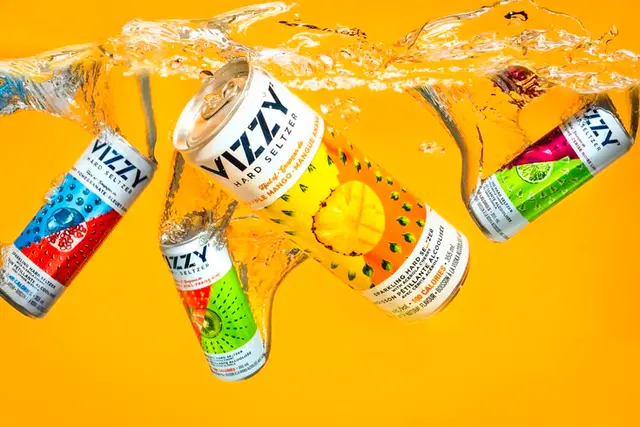 VIZZY hard seltzer cans splashing in studio with bright orange backdrop