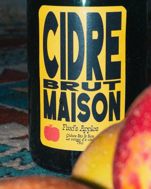Close-up of glass bottle with yellow 'CIDRE BRUT MAISON' label and apple