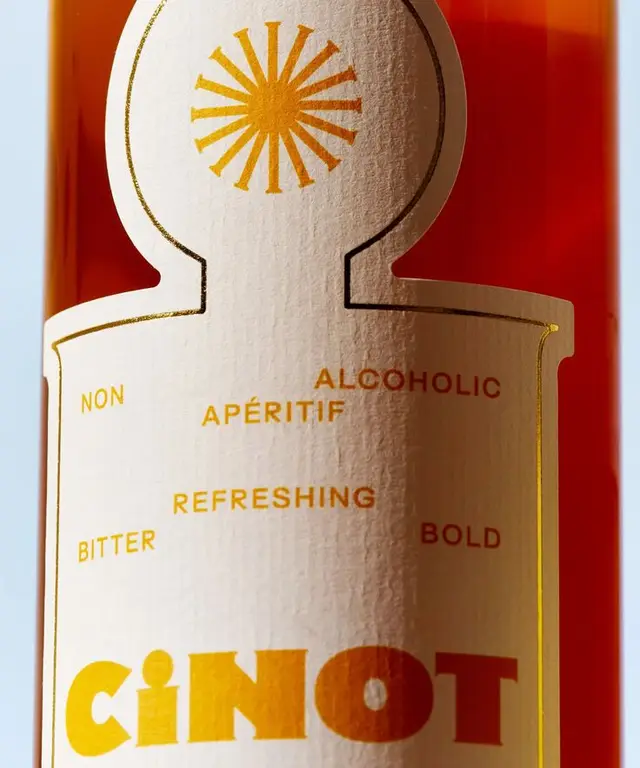 Close-up amber aperitif bottle label with gold foil sunburst — CINOT