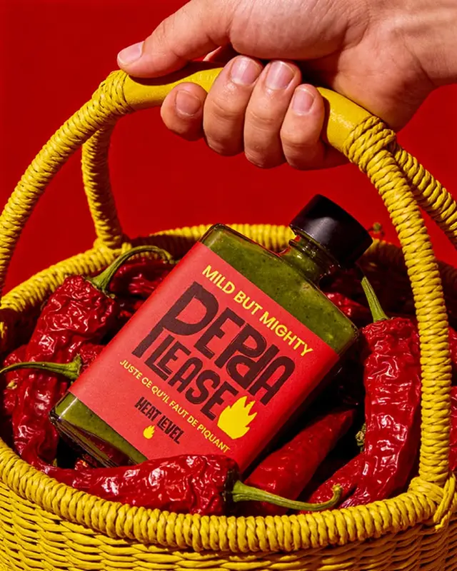 Green 'PEPA PLEASE' hot sauce in yellow wicker basket with dried red chilies
