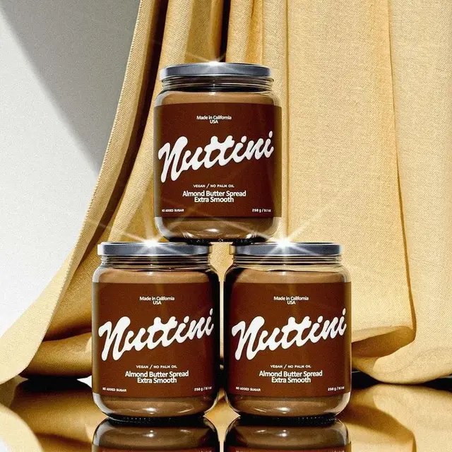 Nuttini Almond Butter Spread — three glass jars stacked on gold fabric backdrop