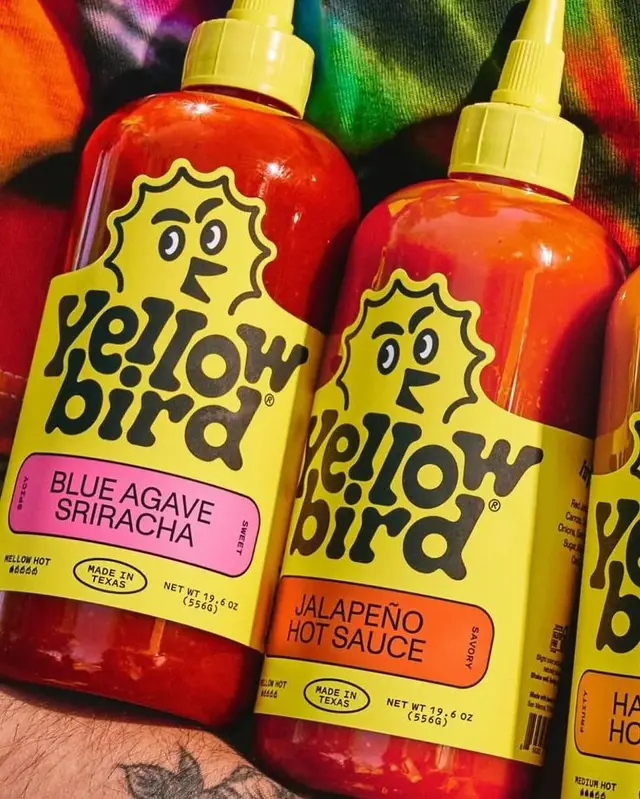 Yellow Bird Blue Agave Sriracha & Jalapeño Hot Sauce bottles on tie-dye fabric