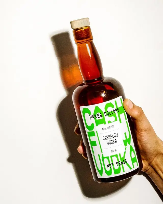 Amber vodka bottle with neon-green 'Cashflow Vodka' label held against white background