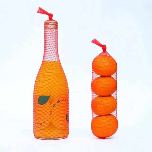 Orange bottle wrapped in red produce netting beside stacked oranges in net bag
