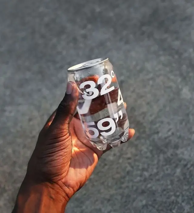 Transparent plastic can with bold white numeric typography ('32° 4 69"') held in hand
