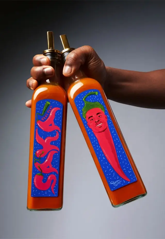 Two tall glass hot-sauce bottles with illustrated chili labels