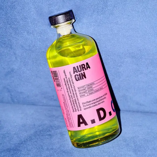 AURA Gin bottle with pink label and neon yellow liquid on blue fabric