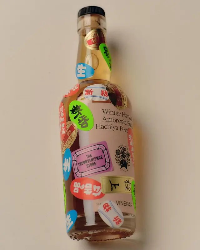 Glass vinegar bottle covered in colorful Japanese stickers — "THE INCONVENIENCE STORE" tag