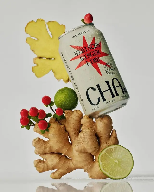 CHA Hibiscus Ginger Lime can balanced on fresh ginger root — studio still life
