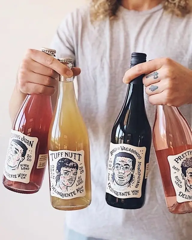 Four Delinquente Wine Co. bottles held forward — illustrated portrait labels