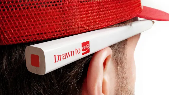 Coca‑Cola 'Drawn to' promotional pencil behind red trucker cap