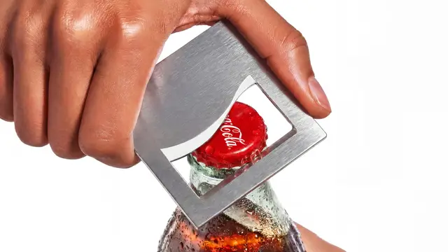 Coca-Cola glass bottle being opened with a stainless-steel opener — close-up