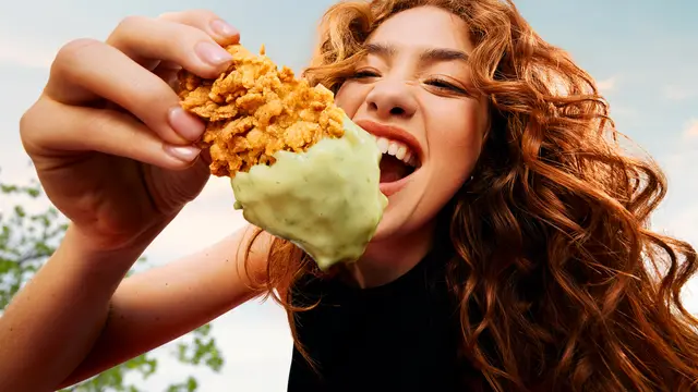 Close-up: KFC crispy chicken tender dipped in pale green sauce