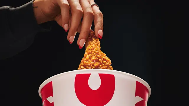 KFC packaging — close-up of fried chicken lifted from white bucket with bold red graphic
