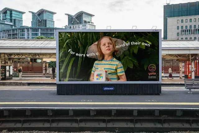 Yoto transit billboard — child holding Yoto audio player at train station