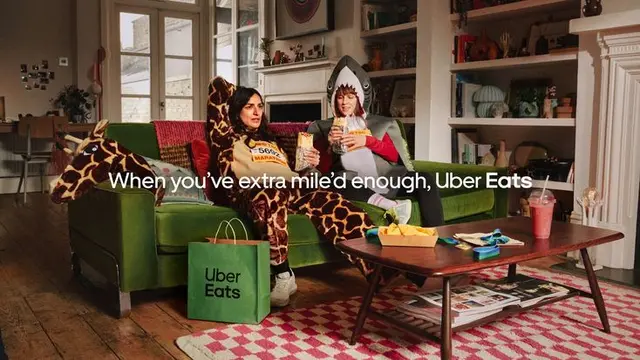Uber Eats campaign still — two people in giraffe and shark onesies on green sofa (Sophie G