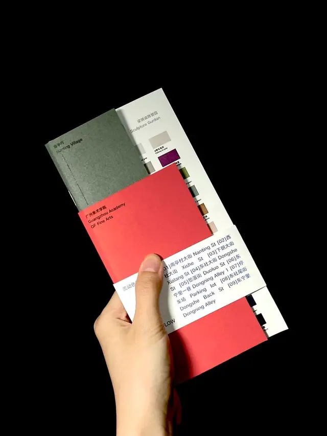 Hand holding stacked brochures with red cover and white typographic band