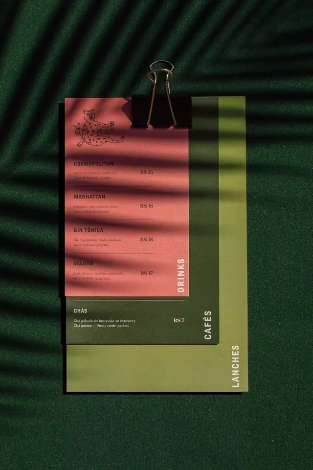 Stacked coral-pink and olive paper menus clipped on dark green felt with striped shadows