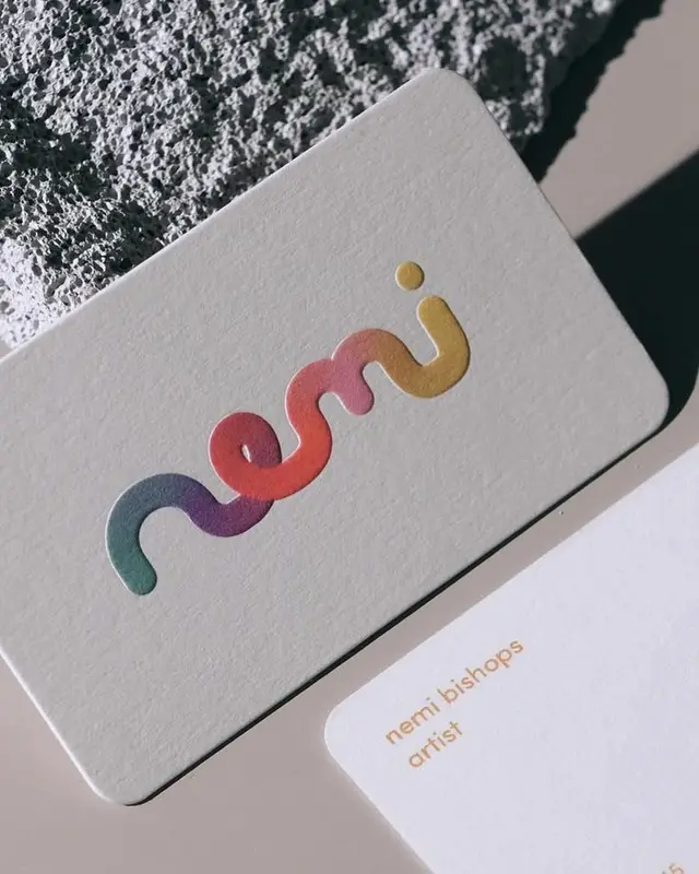 Embossed rainbow-foil 'nemi' business card on textured concrete