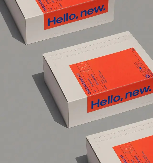 White paperboard onboarding boxes with bright orange sleeve reading "Hello, new."