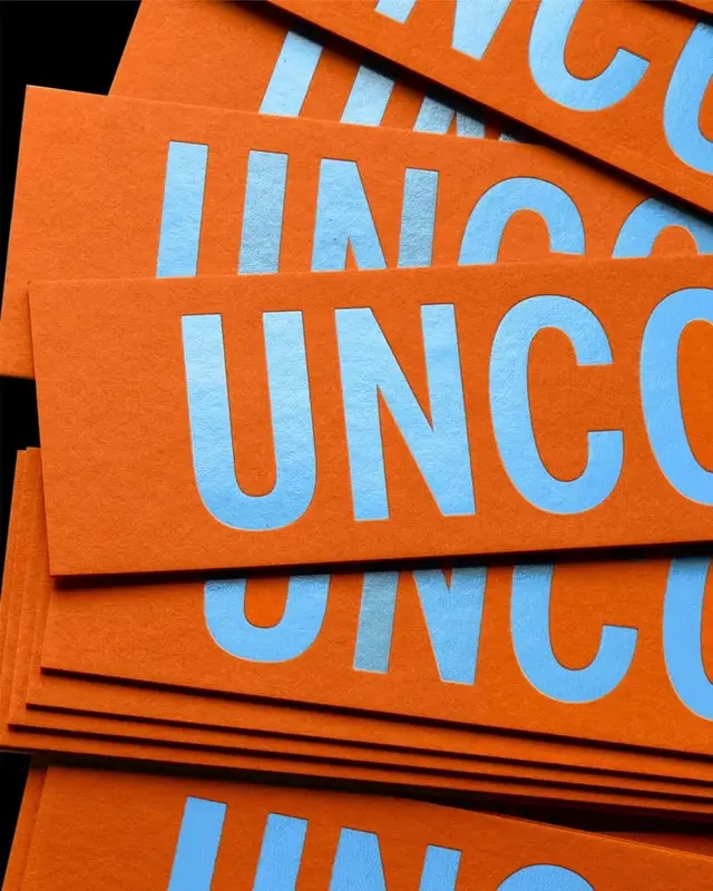Stacked orange cardstock strips with large pale-blue 'UNC' letters