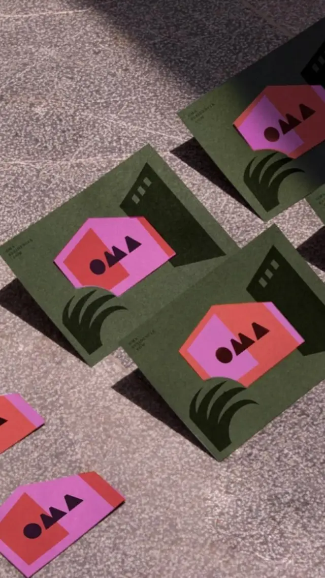 Olive-green printed cards with pink geometric 'OMA' logo — flatlay