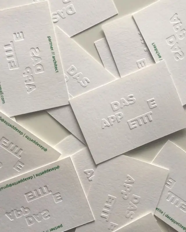 Stacked blind‑embossed white business cards with block lettering ('DAS APP ETIT')