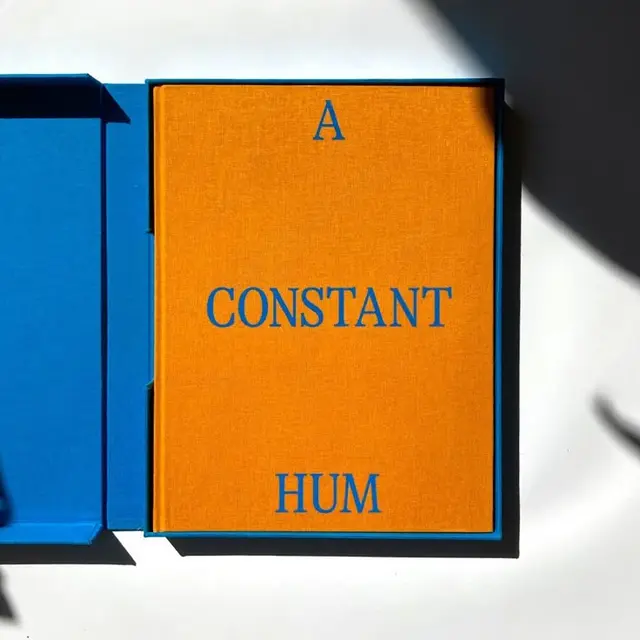 Orange clothbound book 'A CONSTANT HUM' in blue slipcase