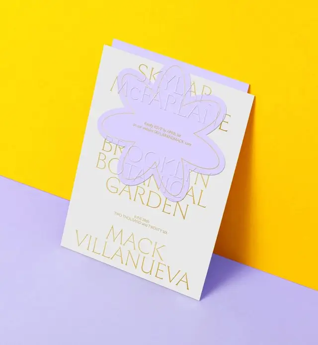 Gold-foil wedding invitation with lavender die-cut flower on yellow and lilac backdrop