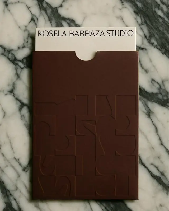 ROSELA BARRAZA STUDIO cream card in blind‑embossed brown sleeve on marble