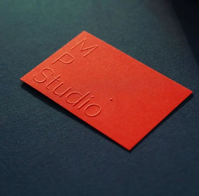 Red blind-embossed 'MP Studio' business card on navy textured paper