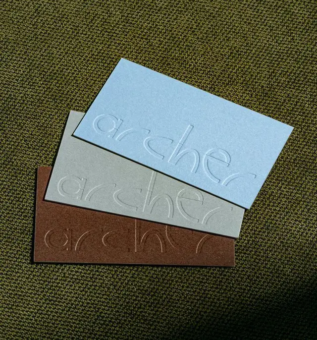 Stacked embossed "archer" business cards on olive-green fabric